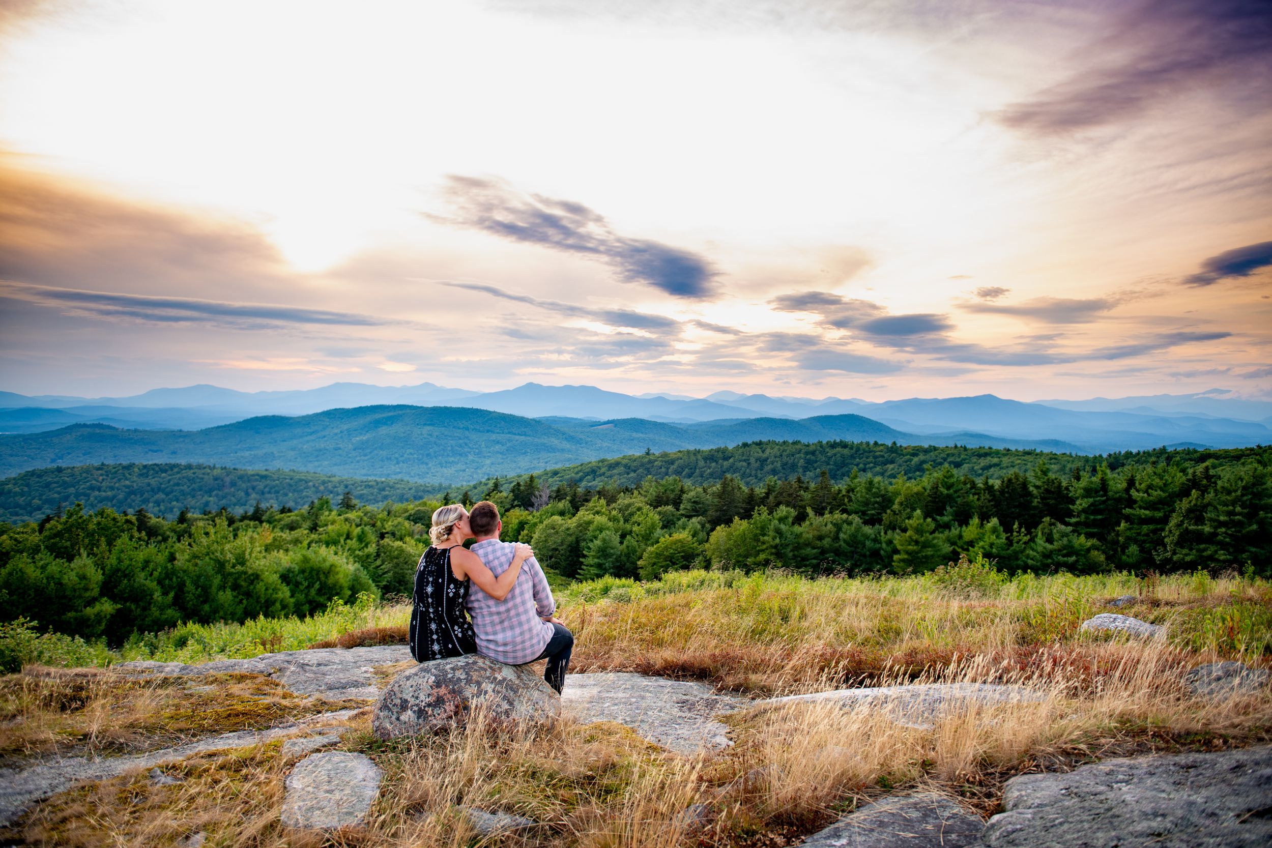 A panoramic mountain landscape at sunset with rolling hills and dramatic clouds.