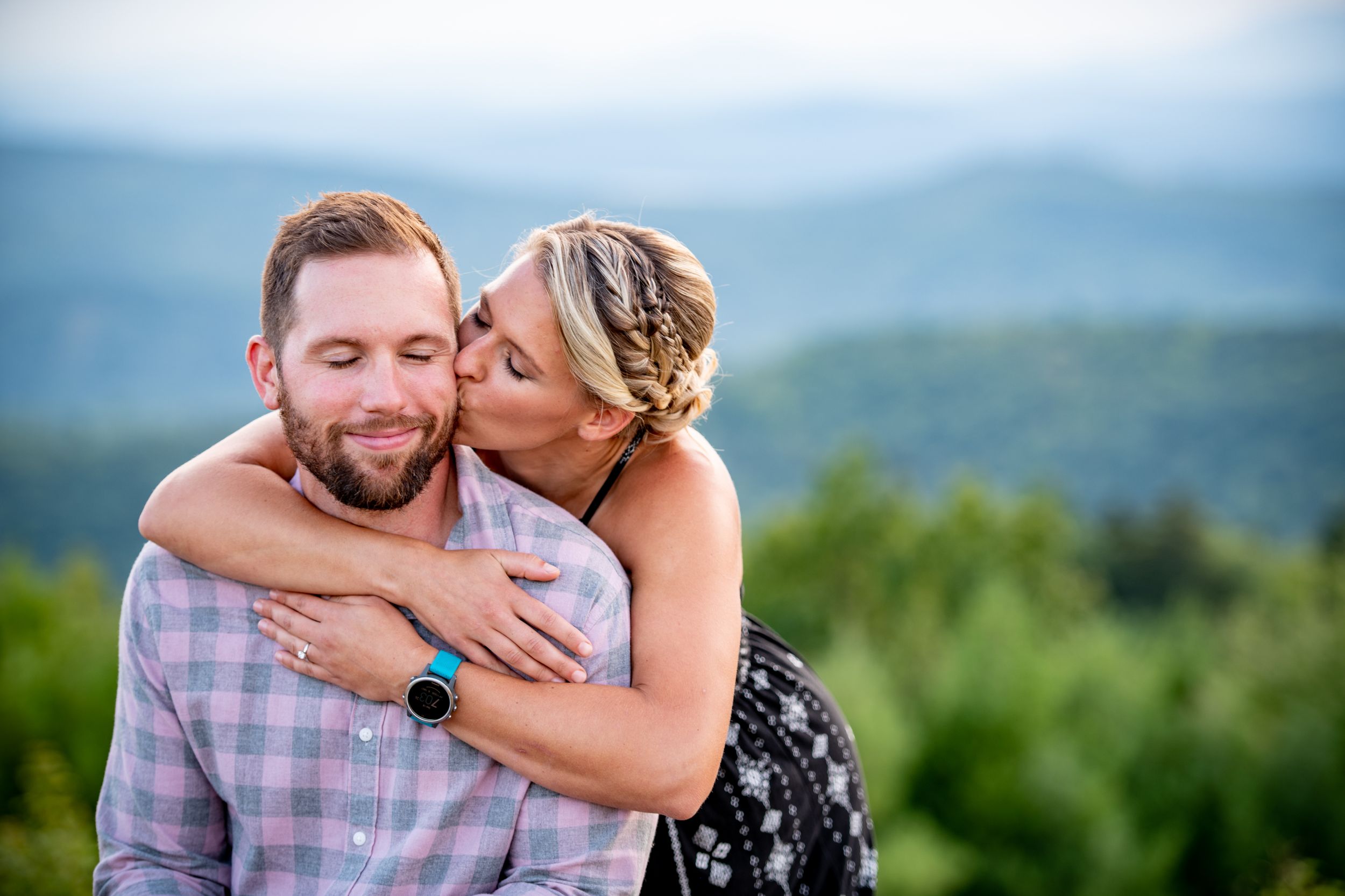 A couple embraces with mountain vistas and blue skies in the background.