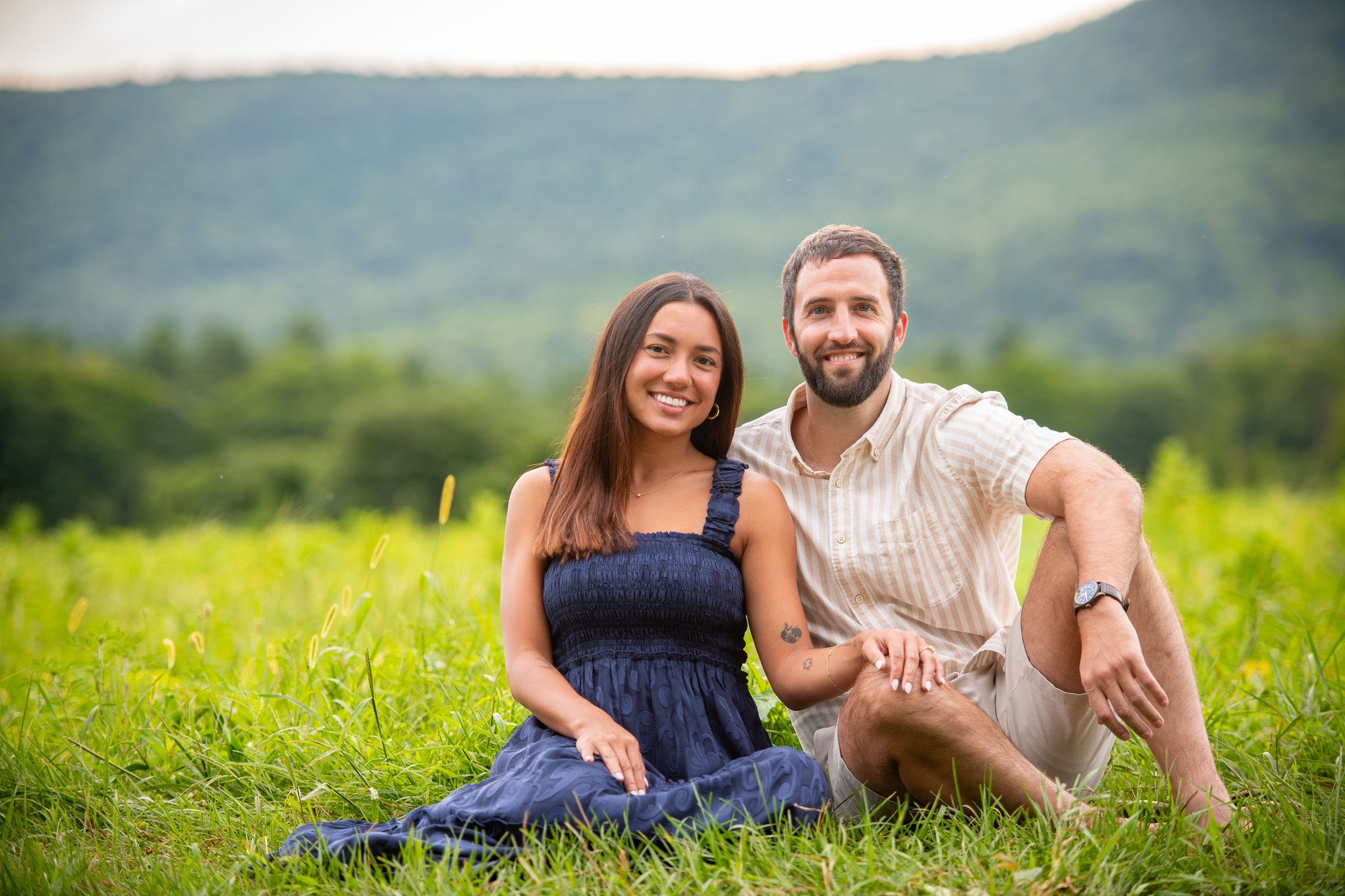 Couple relaxing together in a green field with mountains in the distance.