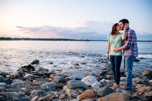 Couple shares romantic sunset moment on rocky beach coastline during golden hour photoshoot.