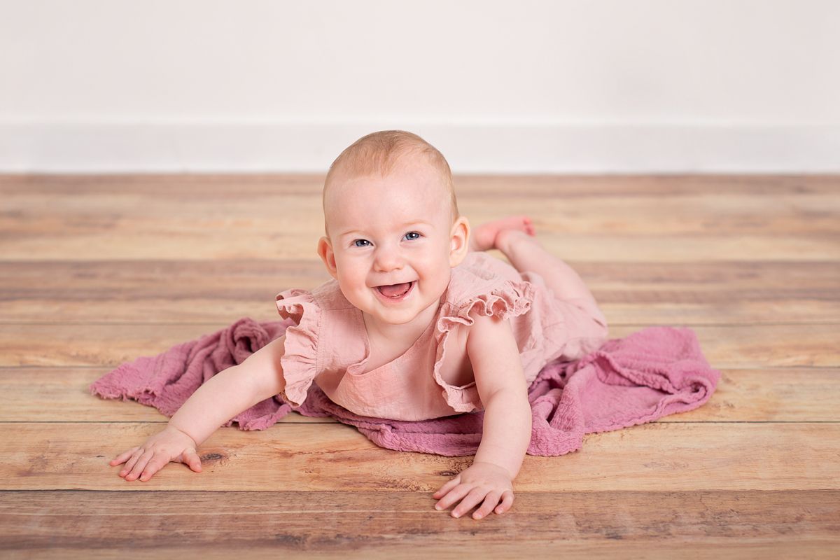 6 month girl pushes up on her hands smiling on a dark wood floor for milestone photoshoot