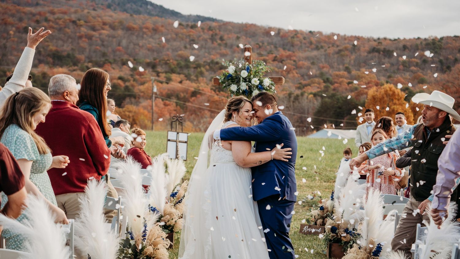 Outdoor autumn wedding ceremony with celebratory confetti toss against mountain backdrop.