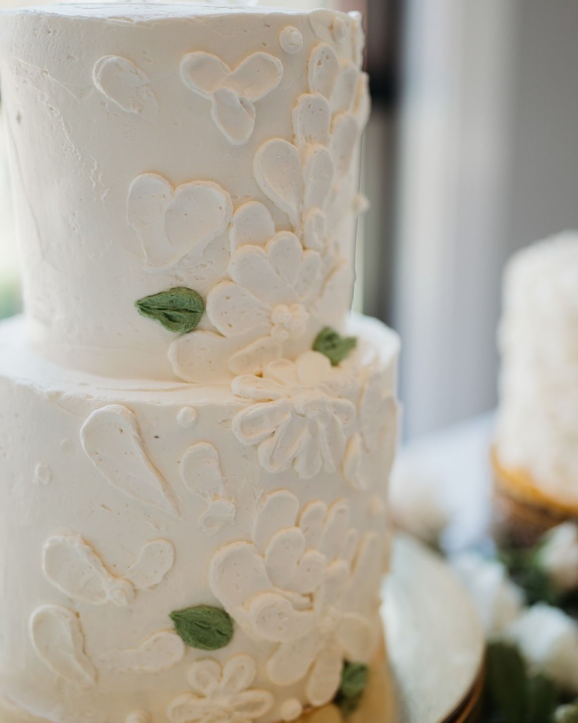 Elegant white wedding cake decorated with delicate heart designs and small green leaves.