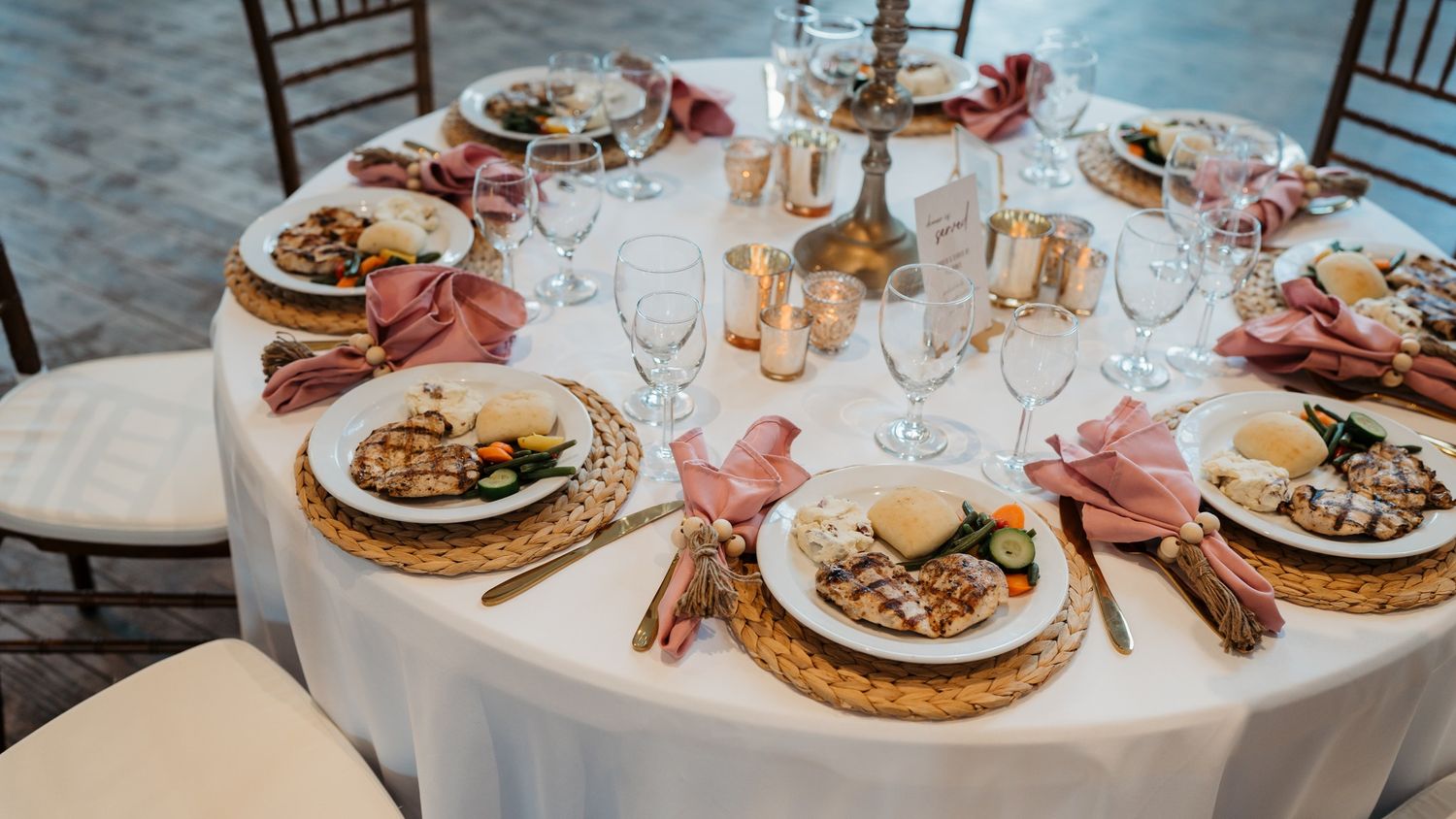 Elegant round dining table set with gold chargers, pink napkins and formal place settings.