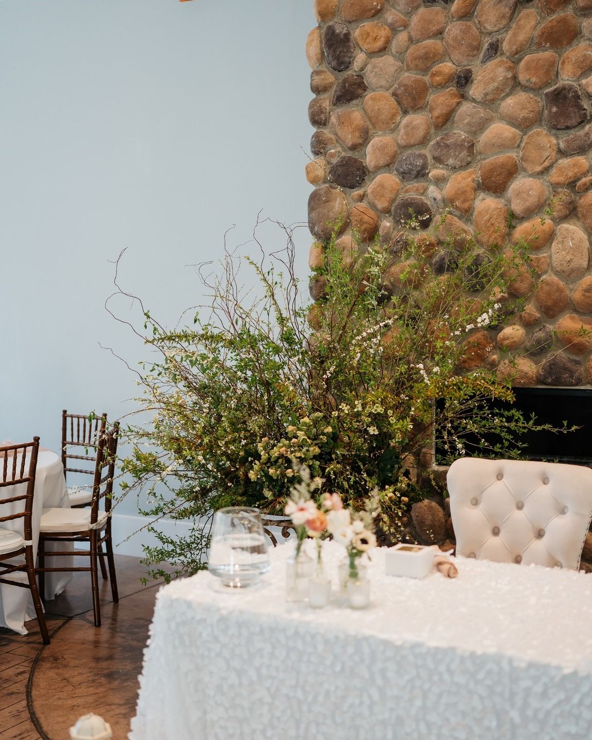 Elegant wedding reception table with white linens and floral arrangements against a stone wall.