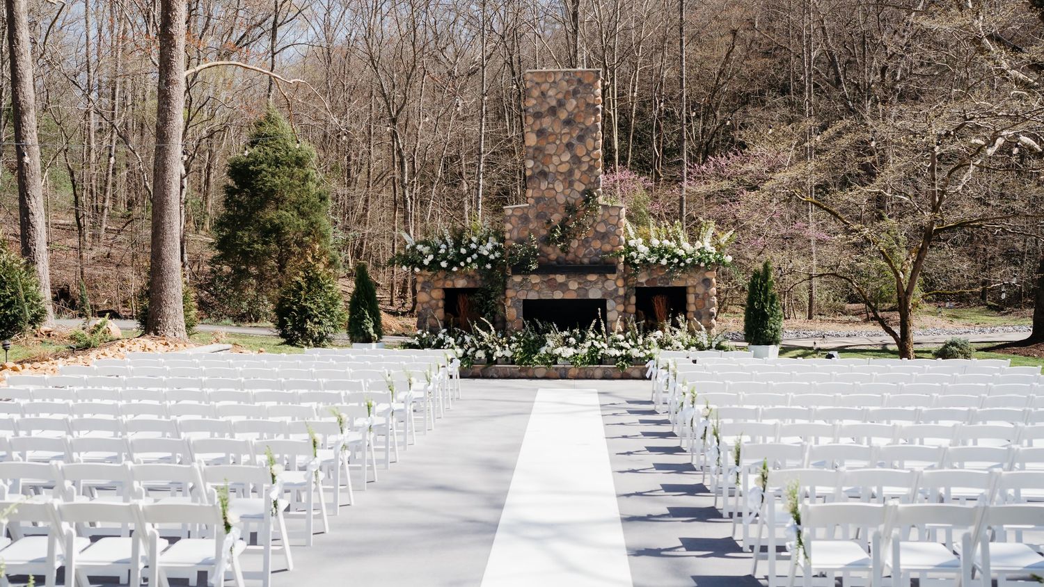 Outdoor wedding ceremony setup with white chairs and aisle runner leading to a stone structure.