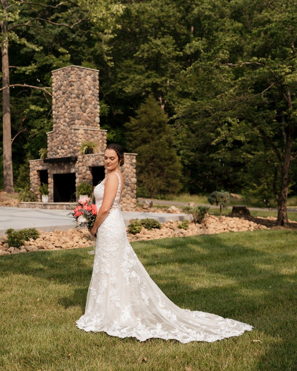 A white lace wedding gown with a long train photographed near a stone fireplace.