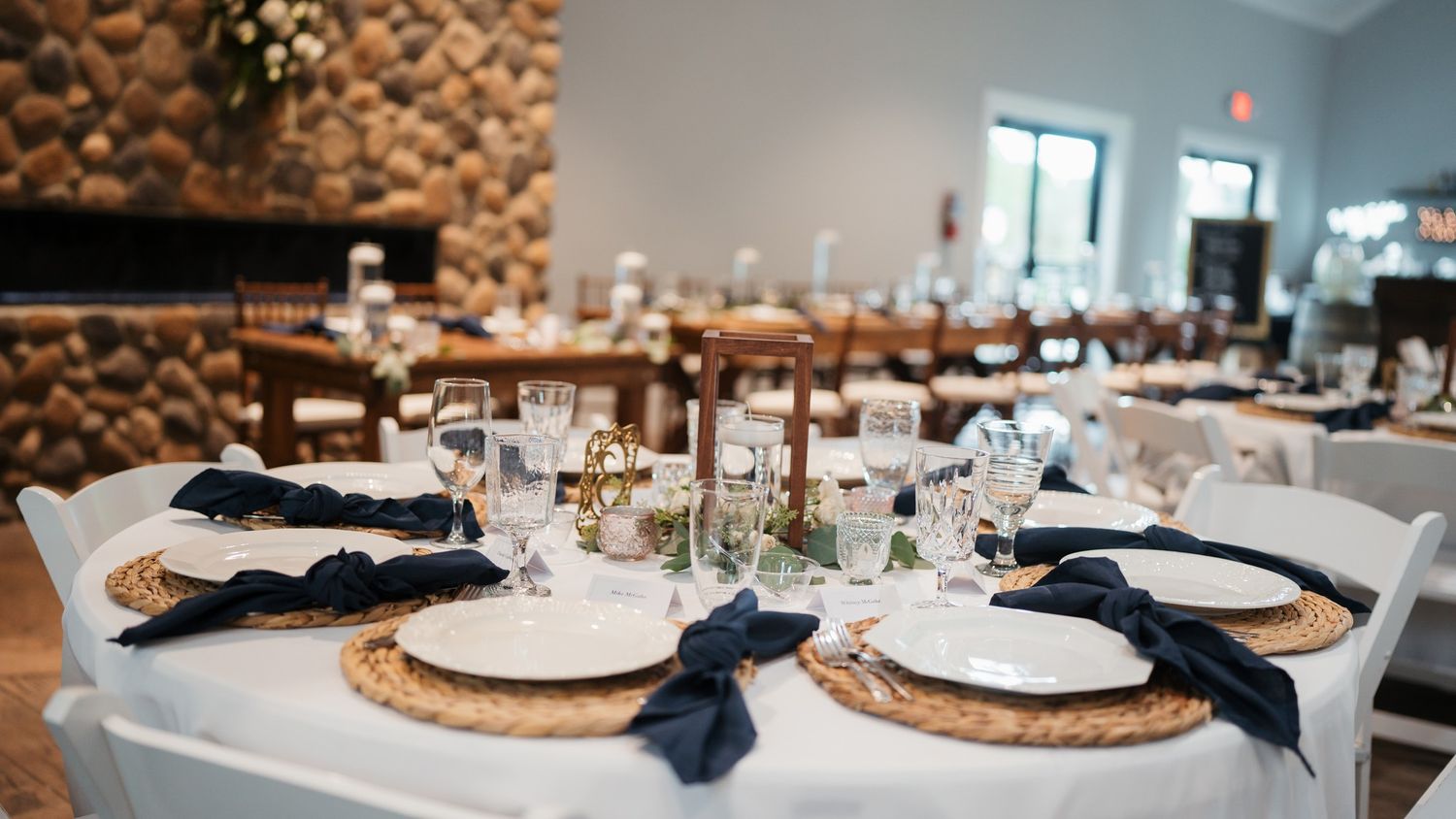 Wedding reception table setting with white linens, navy napkins, and gold charger plates.