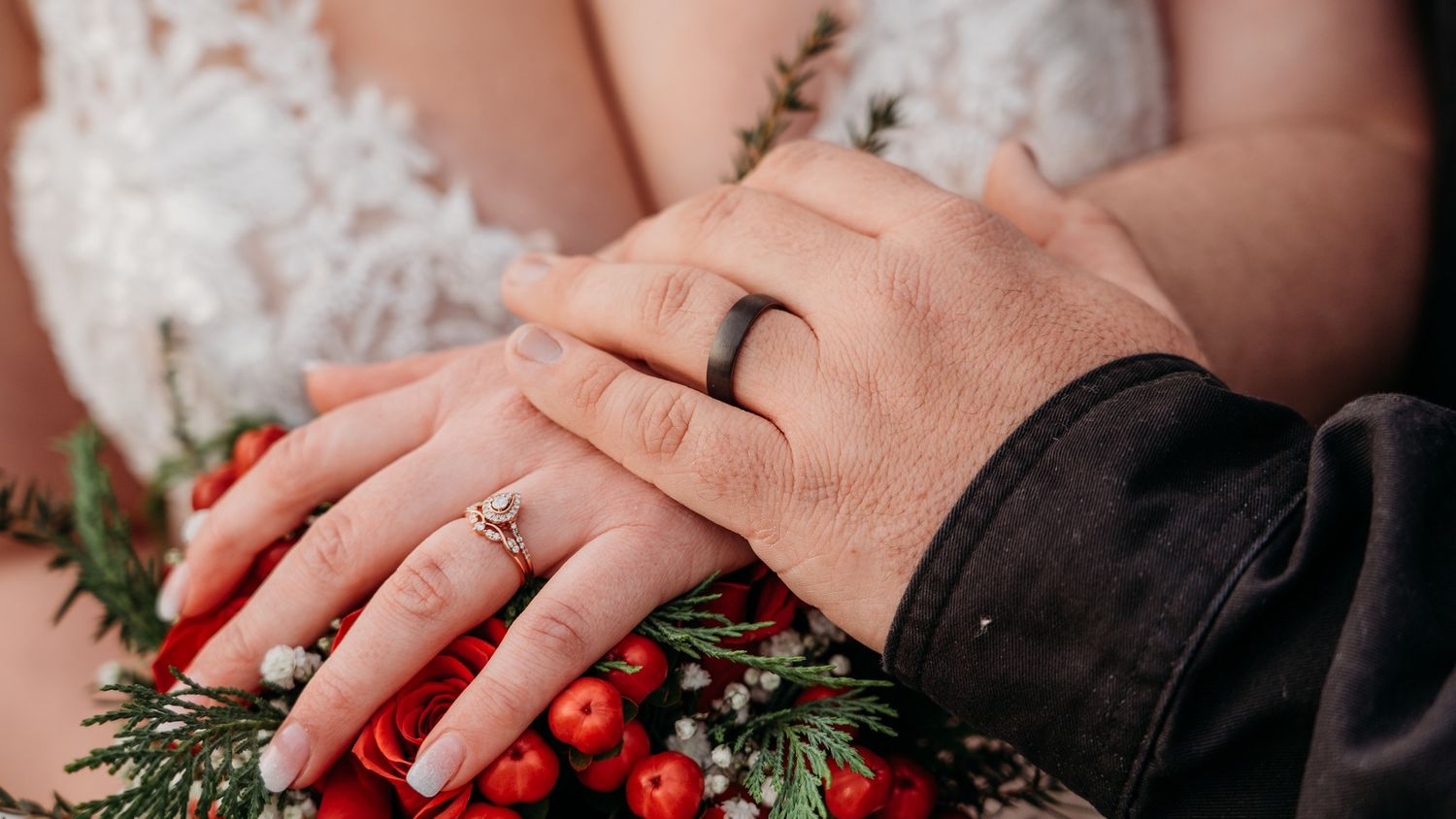 Close-up of wedding rings on hands with winter greenery and red berries.