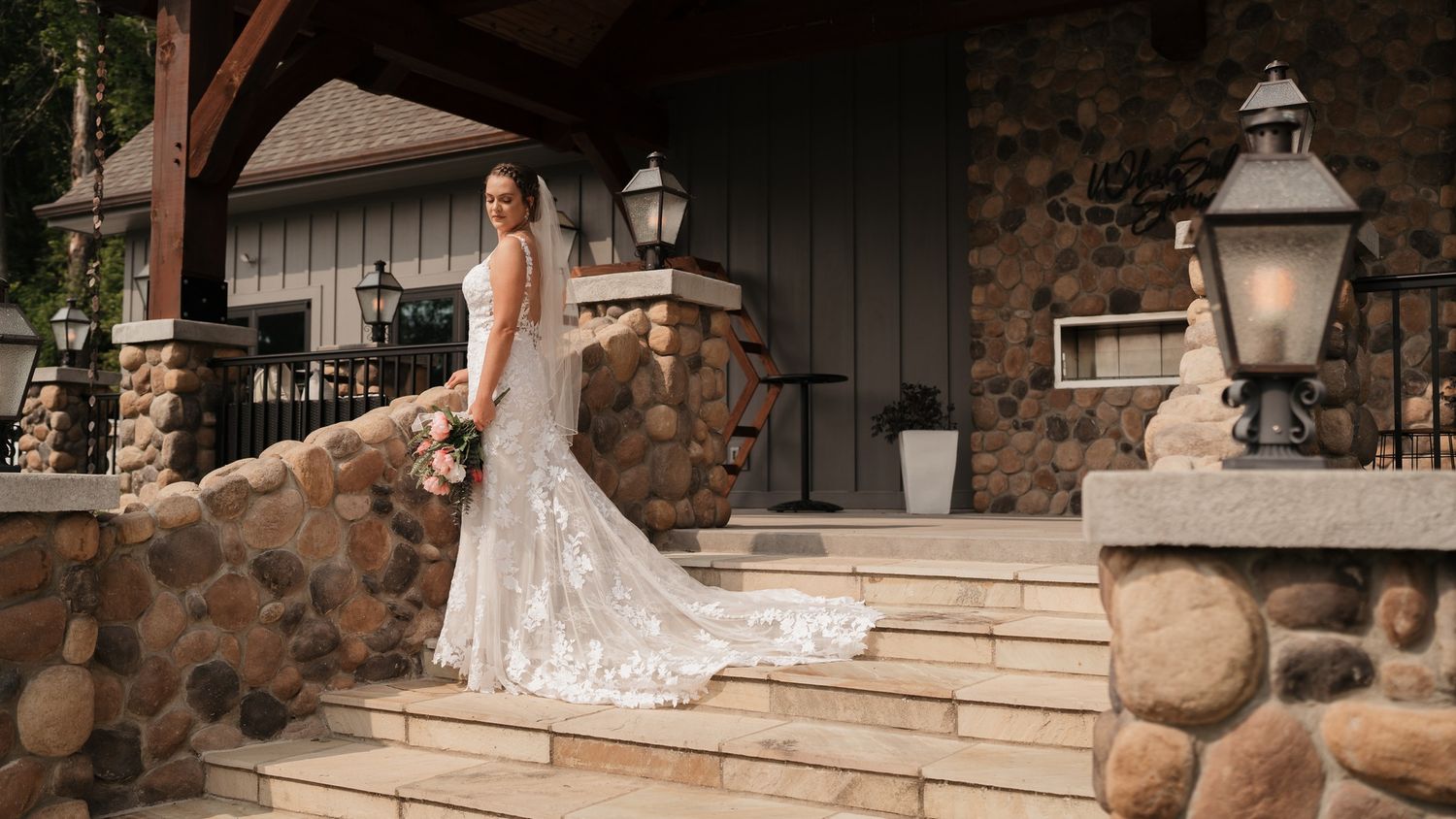 A detailed lace wedding dress with a long train photographed on stone steps with lanterns and rustic architecture.