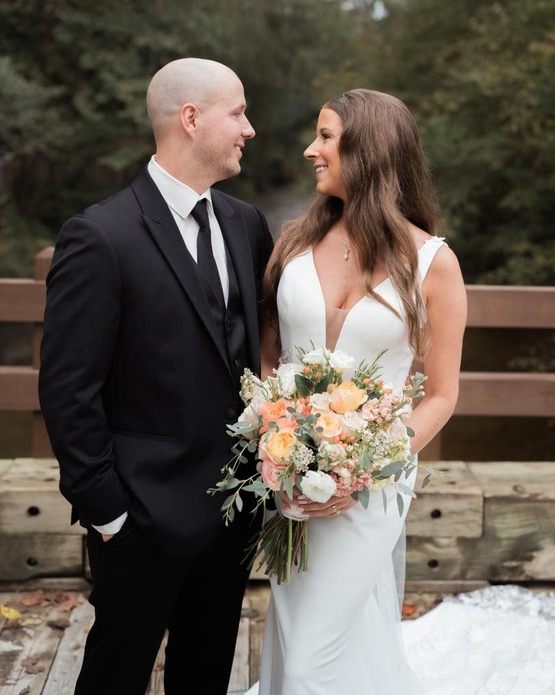 A romantic wedding portrait of a couple in formal attire holding a peach and white floral bouquet.