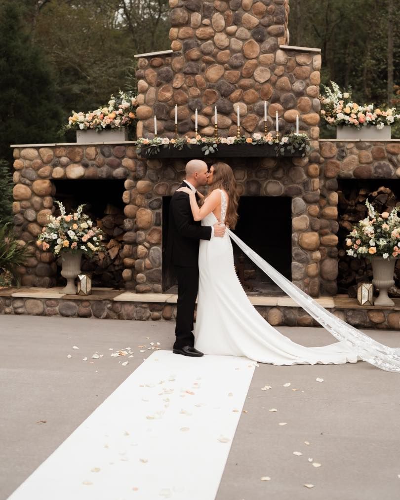 A romantic wedding moment in front of a grand stone fireplace decorated with floral arrangements.