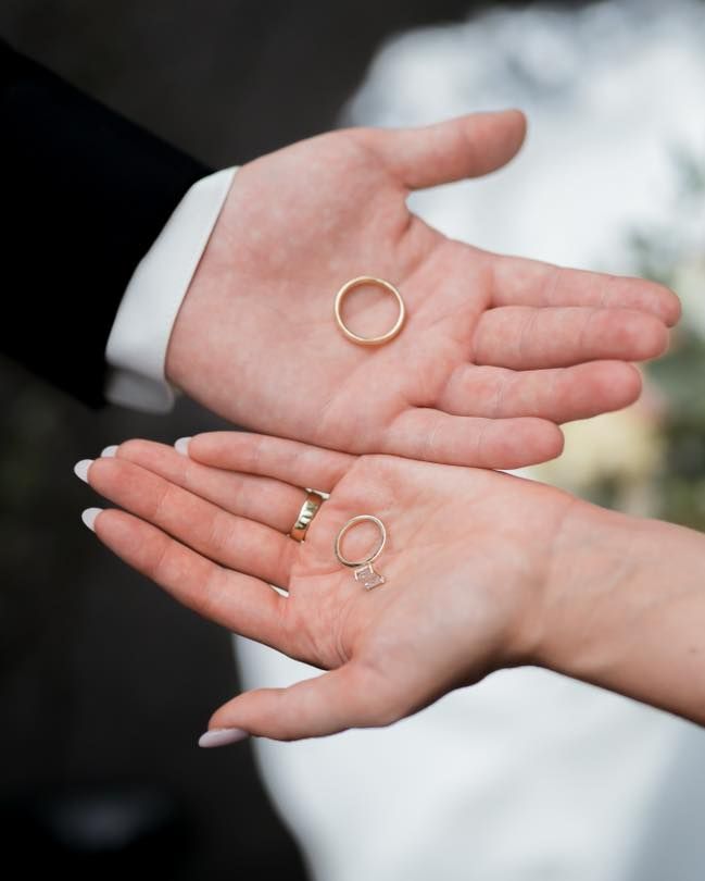 Two hands holding gold wedding rings against a formal attire background.