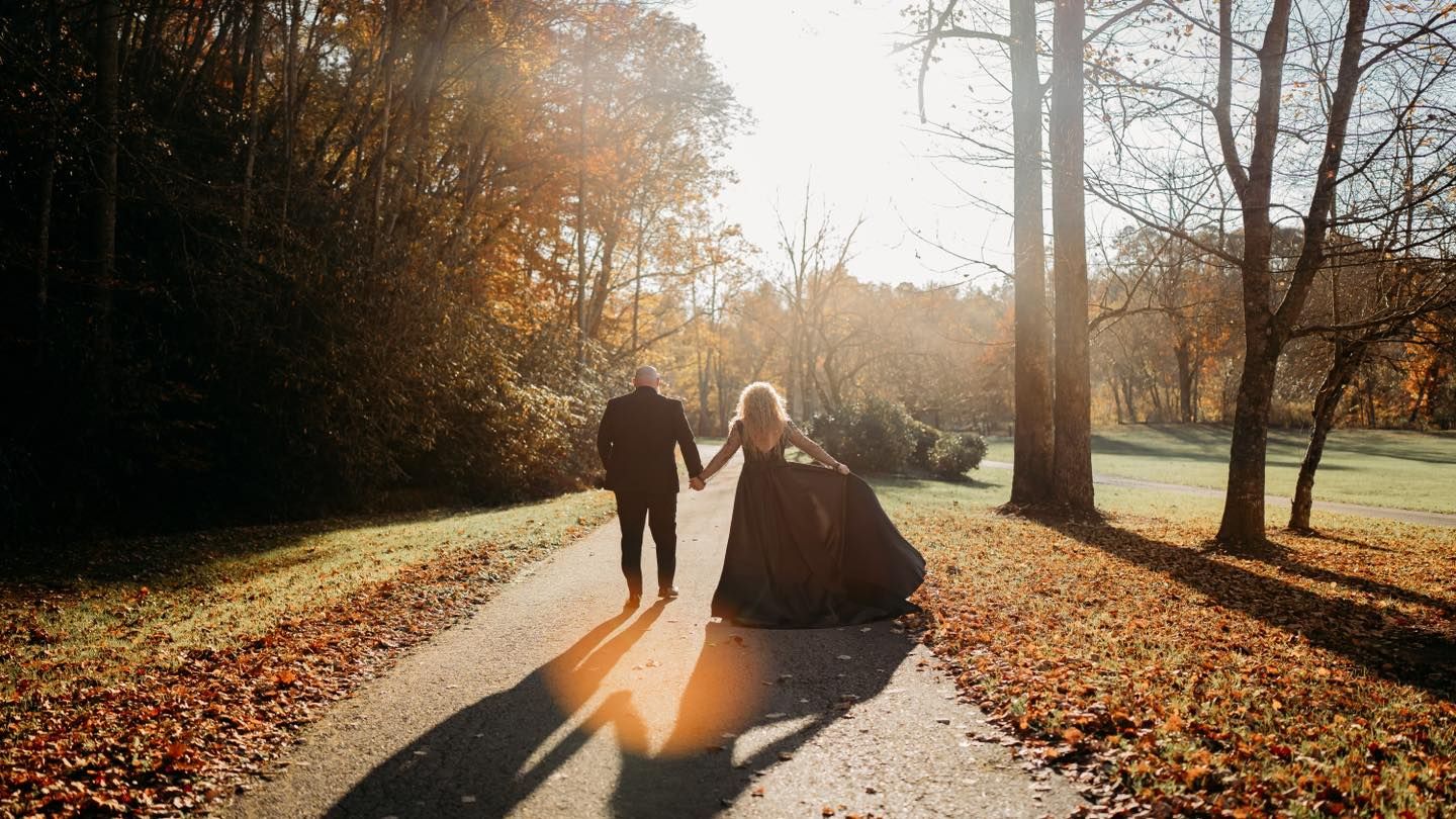 A silhouetted couple walking hand in hand during golden hour on an autumn path.