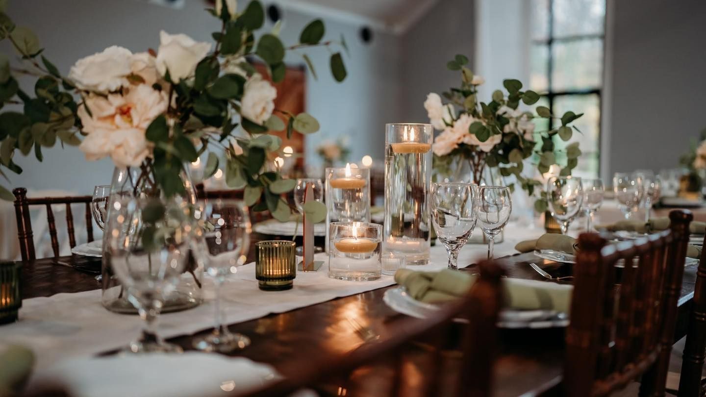 An elegant wedding reception table setting with floral centerpieces, candles, and crystal glassware.