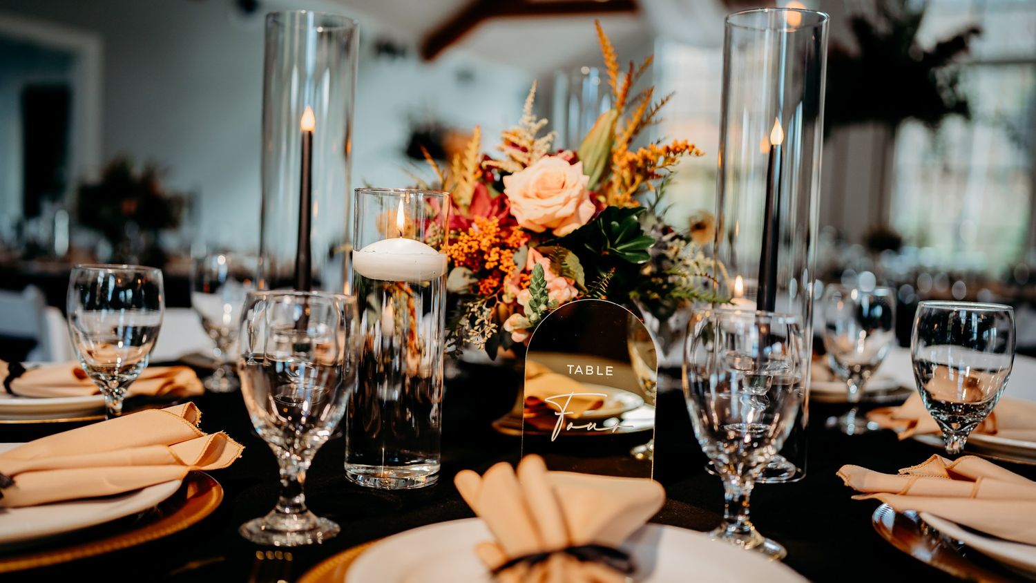 A formal dining table set with orange floral arrangements and glass candle holders for a wedding reception.