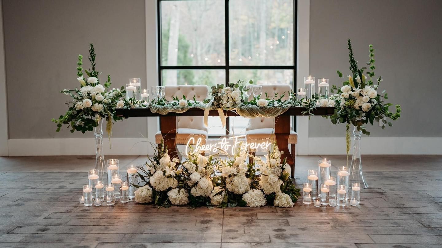 White floral arrangements and candles decorate a sweetheart table at a wedding reception.