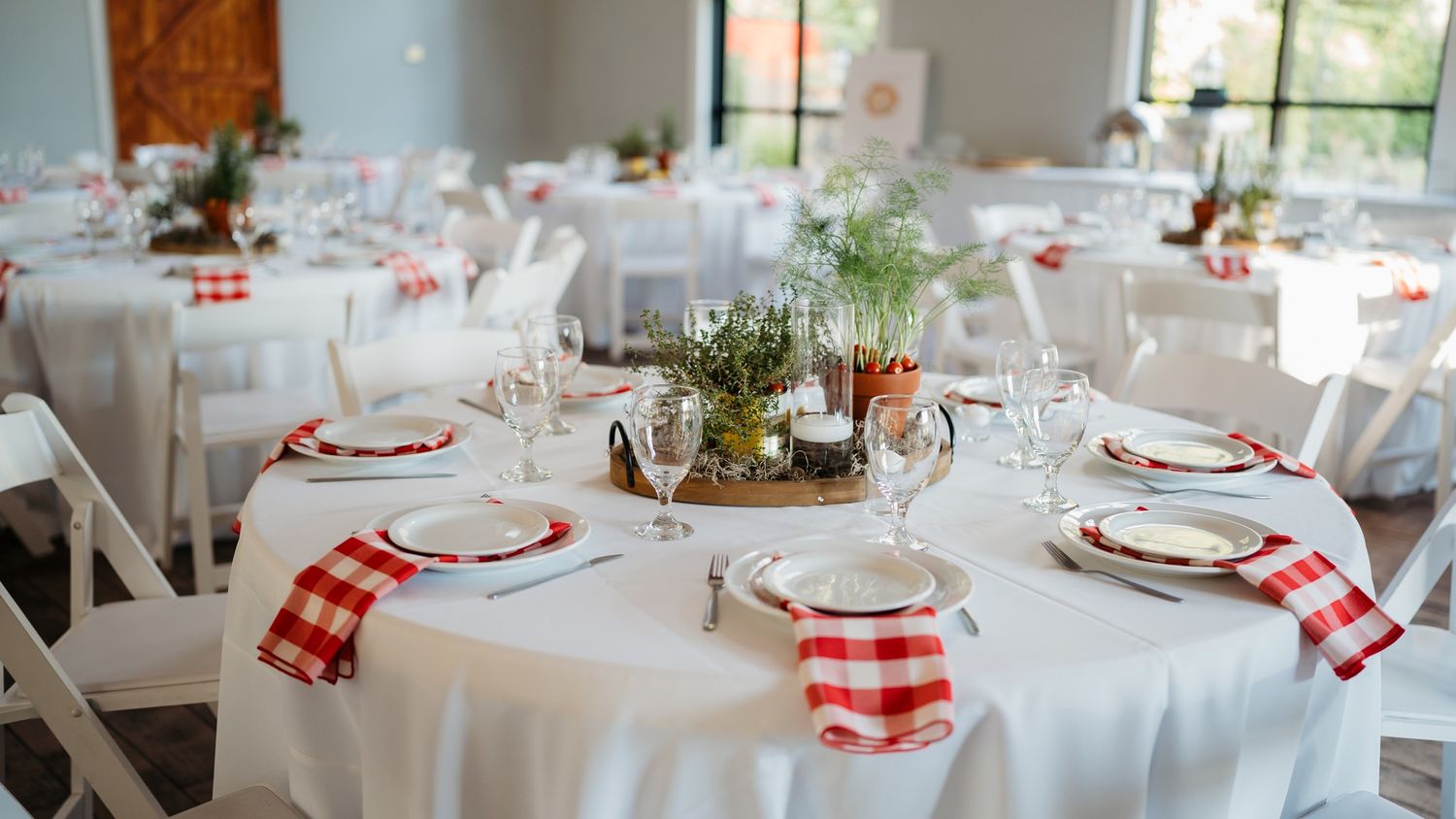 A rustic wedding reception table with red gingham napkins and white tablecloths.