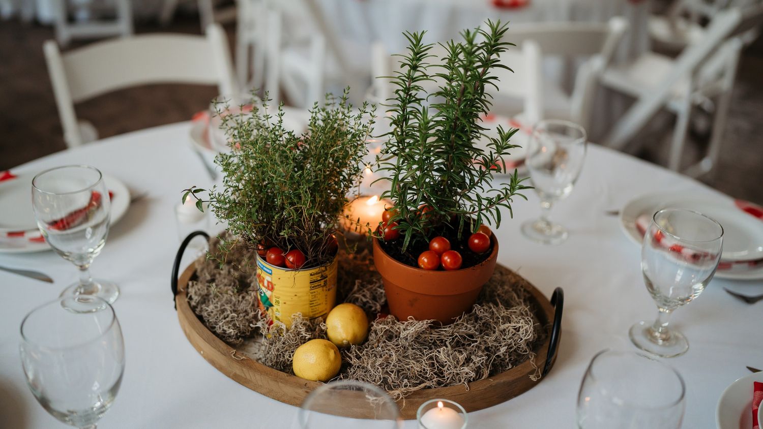 A centerpiece featuring potted herbs, lemons and candles on a round reception table.