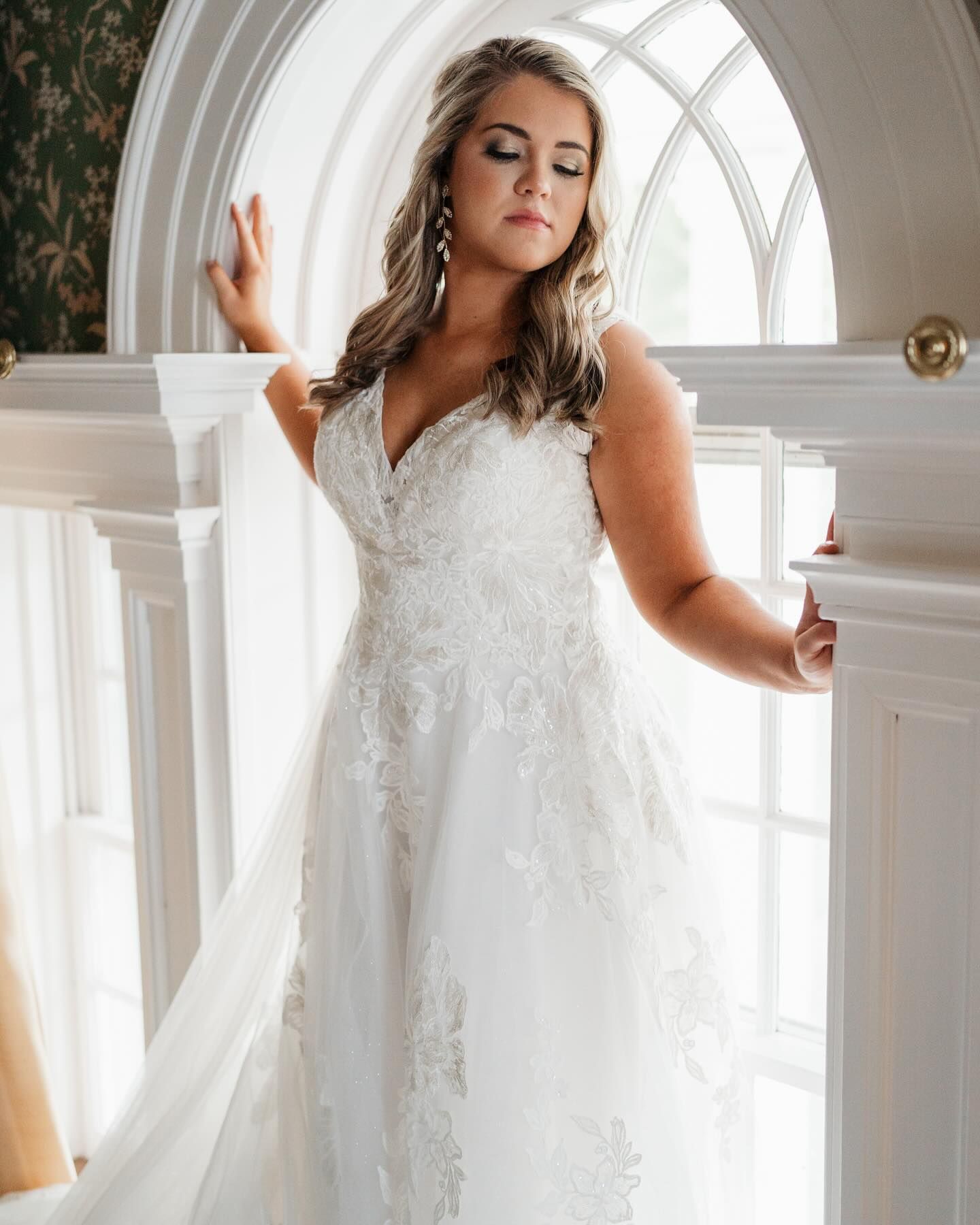 Elegant white wedding dress with lace details and delicate tulle shown in a room with arched window.