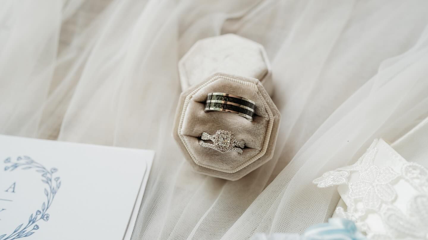 Wedding rings nestled in a grey velvet ring box with invitation details.