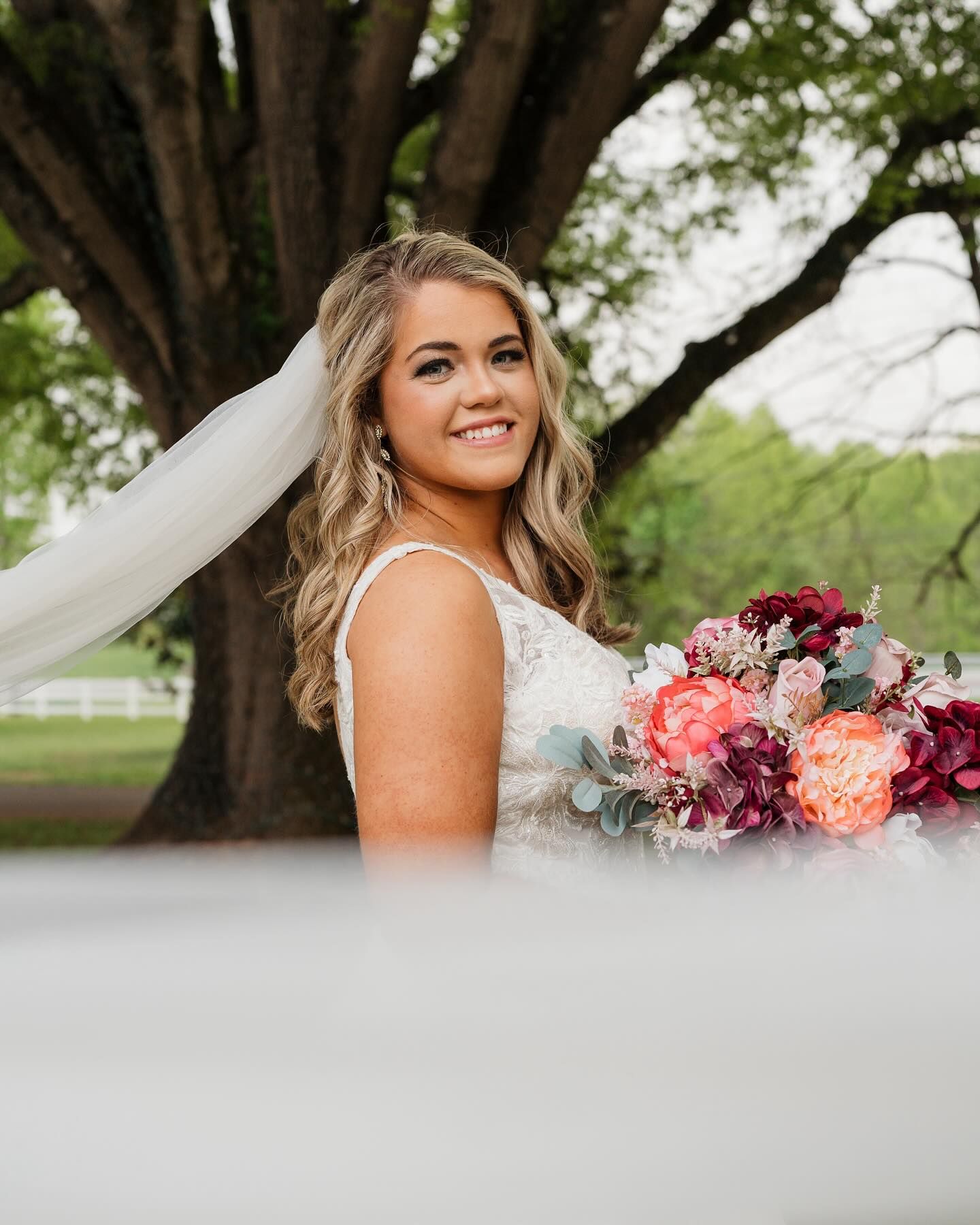 Beautiful bridal portrait outdoors with vibrant pink and burgundy bouquet under a majestic tree.