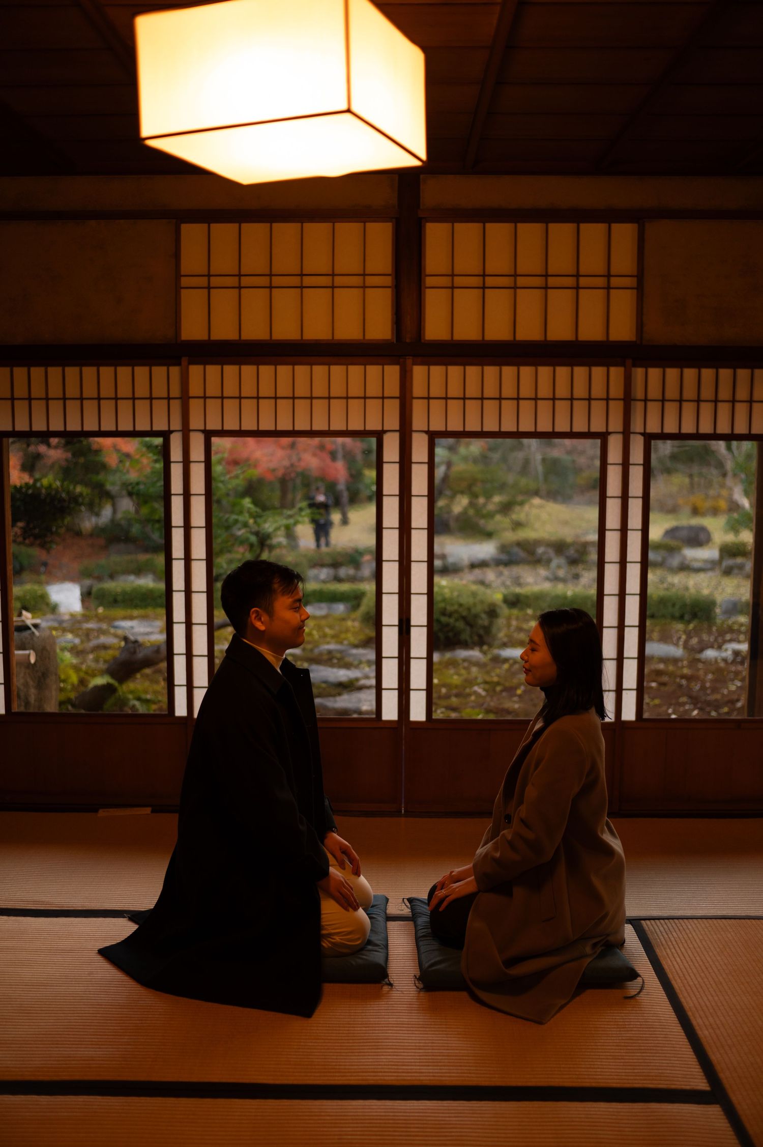 Couple sitting face-to-face on tatami mats in a traditional Japanese room with shoji screens.