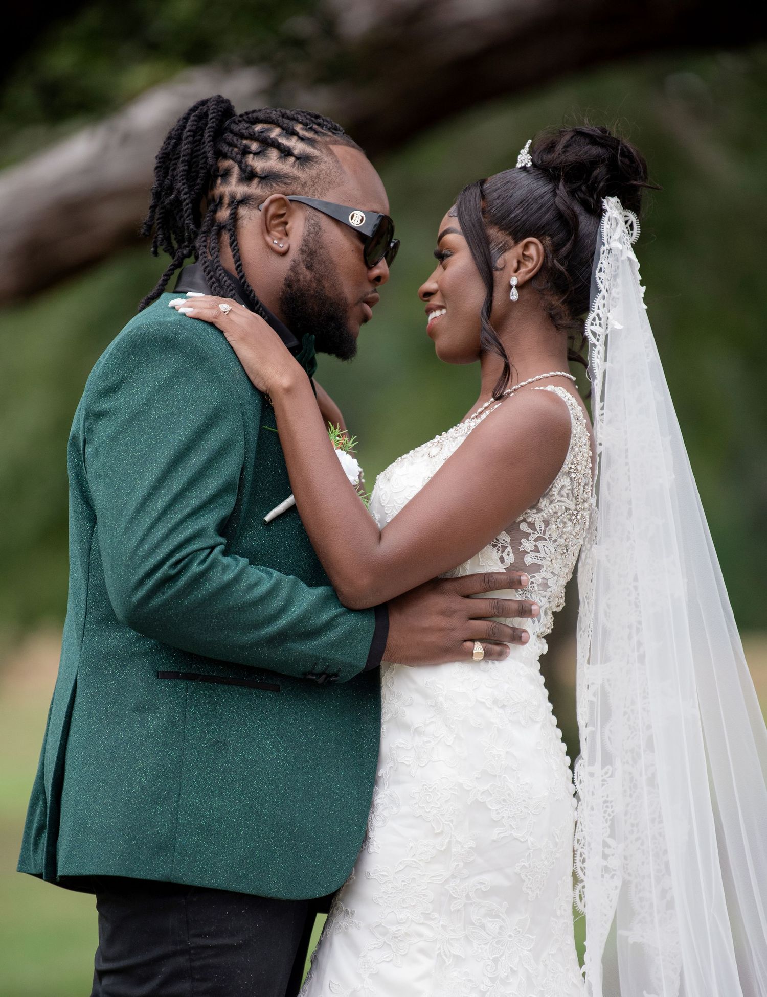 A couple shares an intimate moment on their wedding day, with the bride in white and the groom in a green suit.
