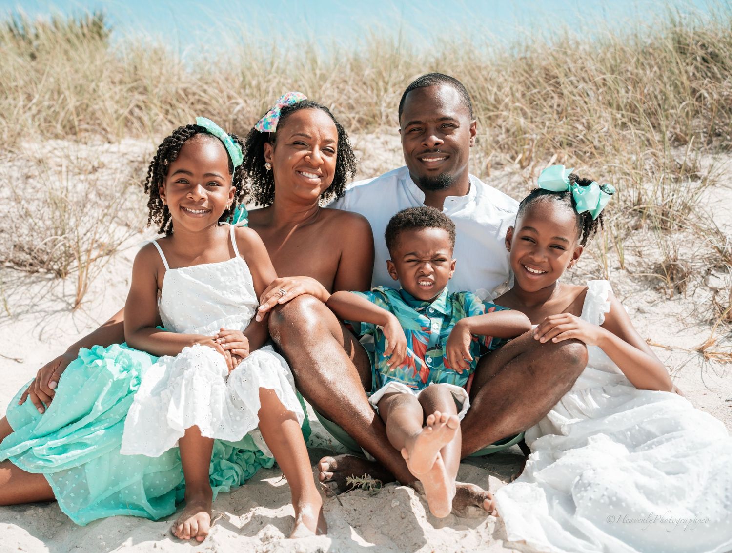 Family shares joyful moments together while sitting on white sand at the beach.