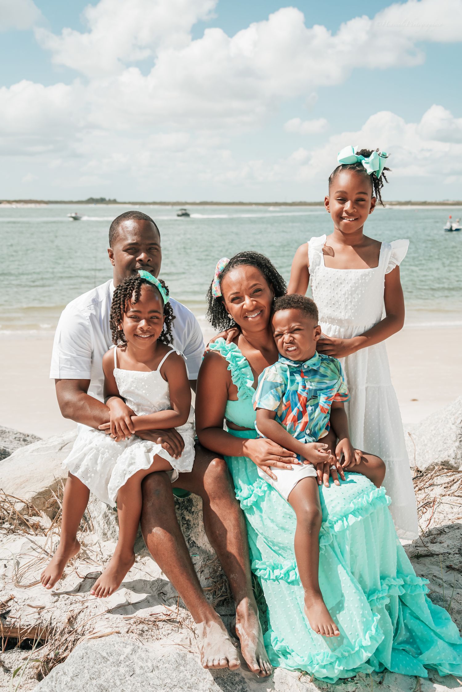 Happy family lounges on beach sand while wearing coordinated mint green and white outfits.