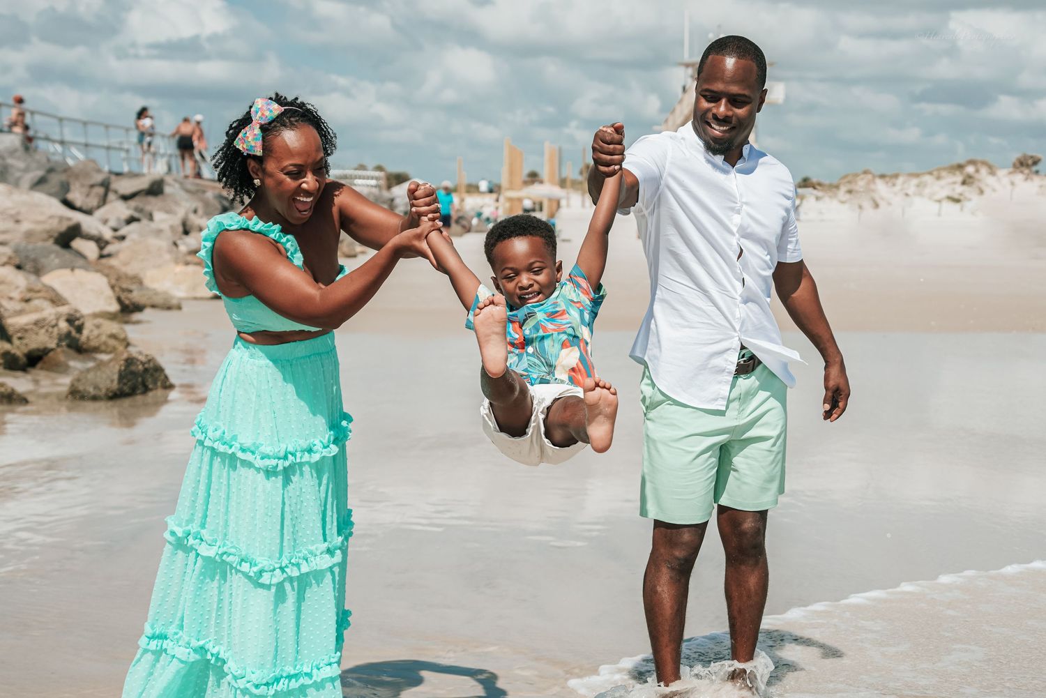 Family runs and plays together along shoreline wearing coordinated beach outfits.