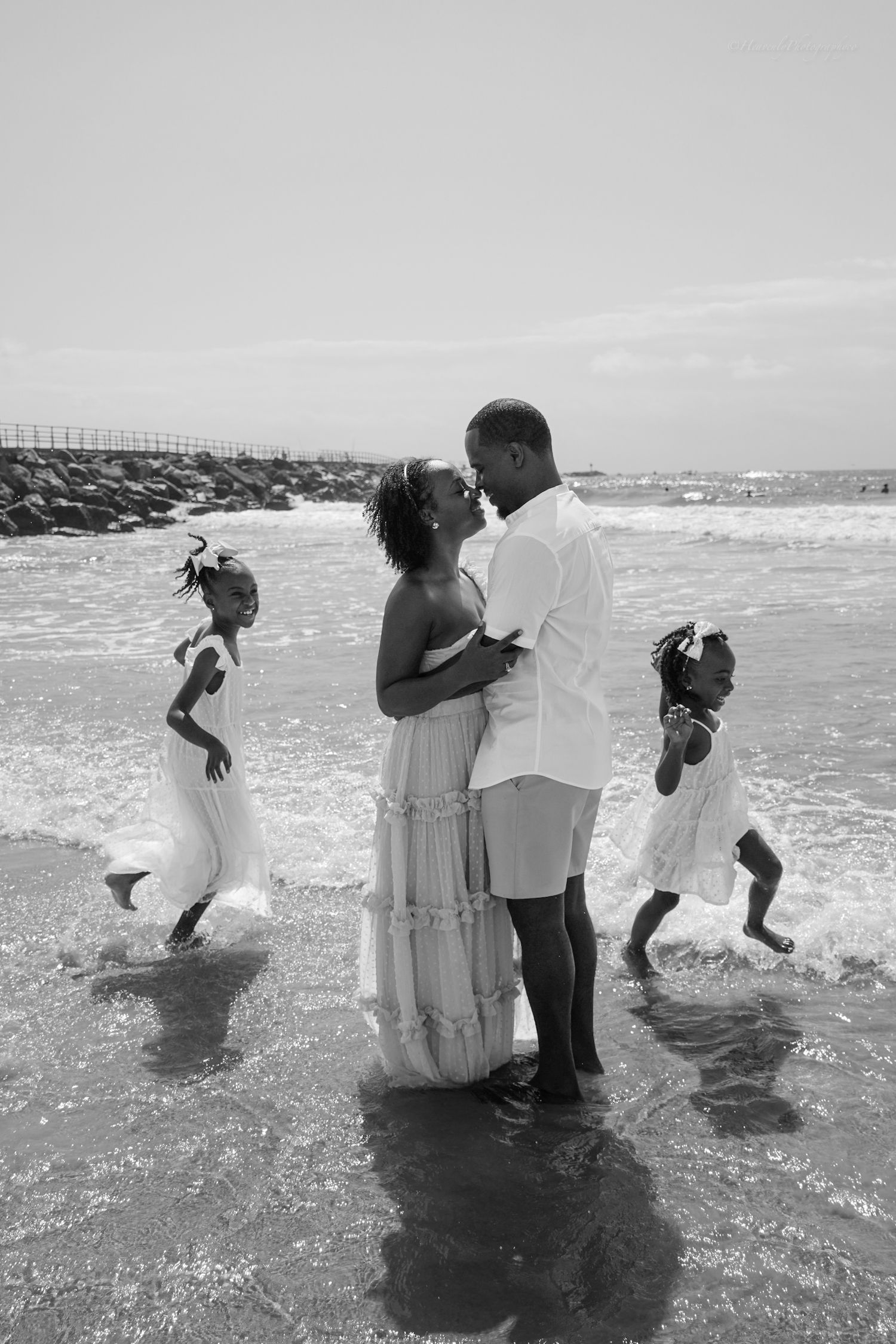 Family enjoying playful moments at the beach in black and white as waves crash around them.