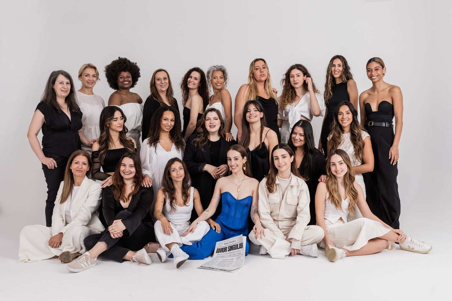 A group of people wearing black and white outfits pose together on a white studio floor for a fashion shoot.