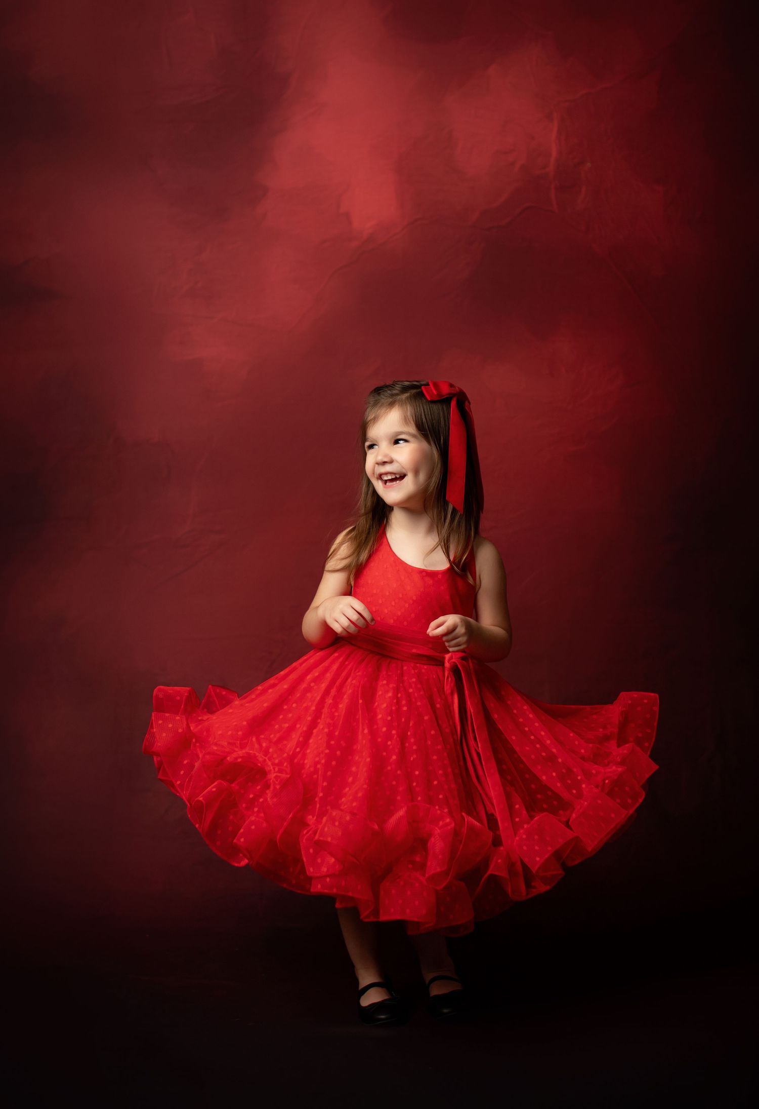 A vibrant red party dress captured against a deep red background in a studio setting.