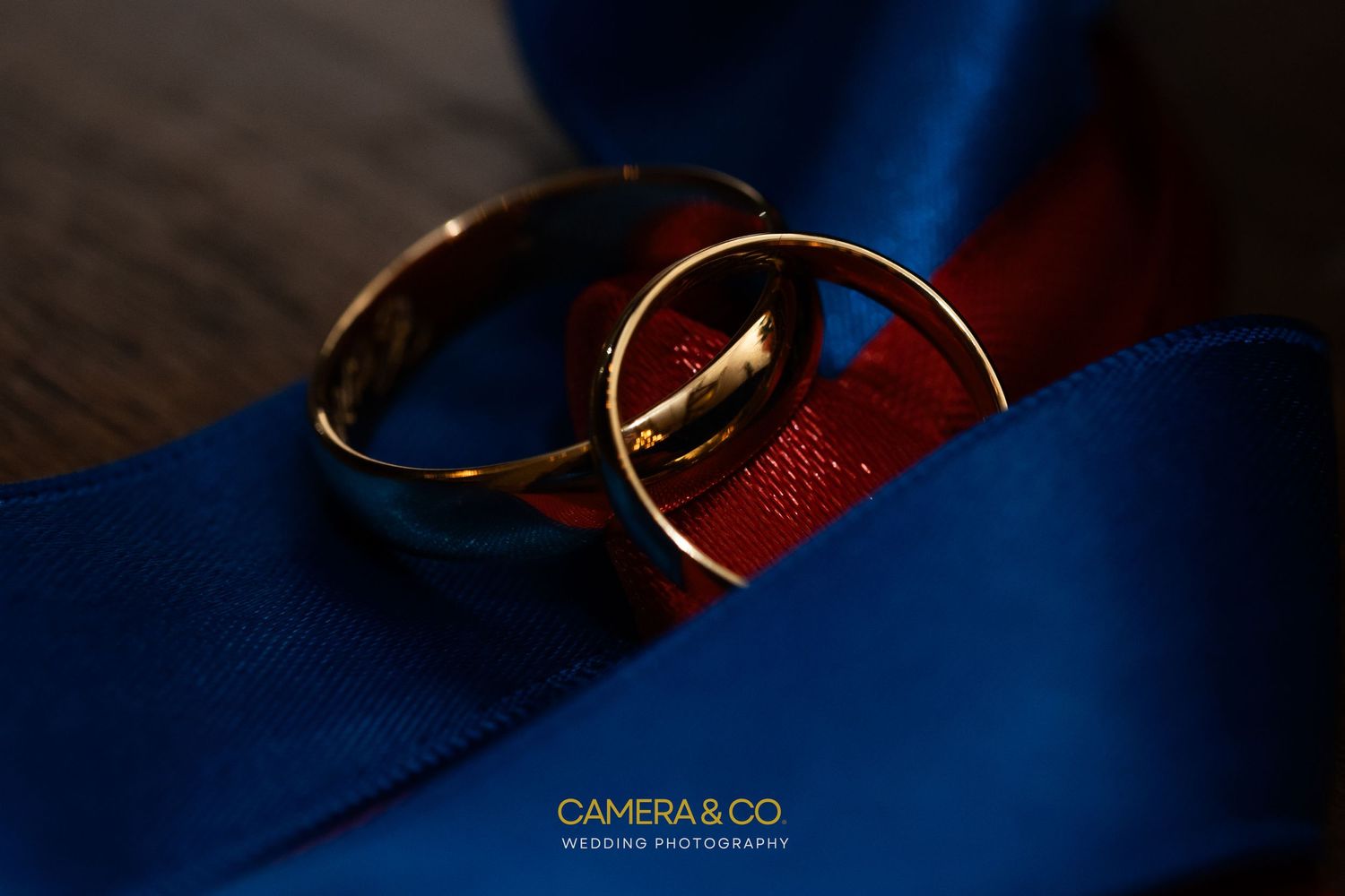 Gold wedding rings photographed with dramatic blue lighting on dark background.