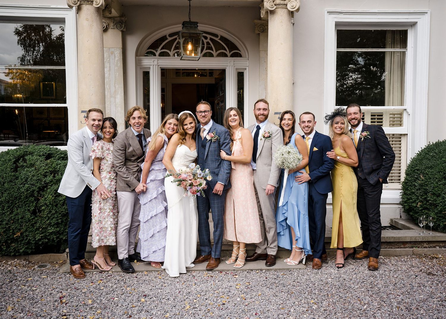 A wedding party poses together outside an elegant white mansion with a grand arched doorway in Halifax, Nova Scotia