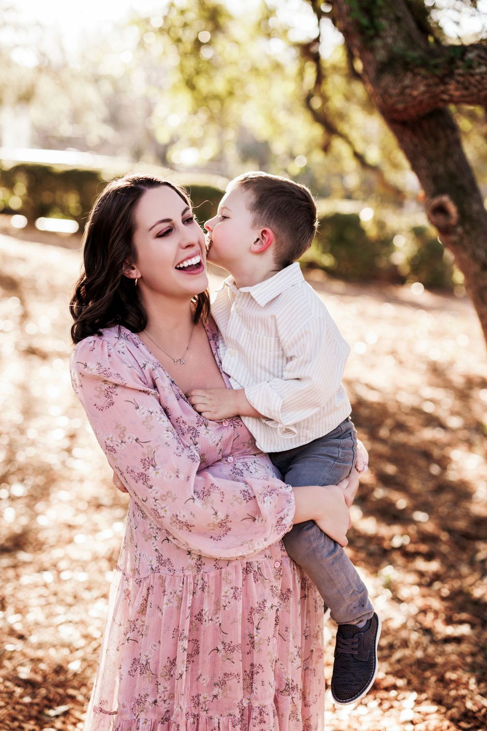 A joyful family moment captured in warm sunlight under autumn trees with a pink floral dress and casual attire.