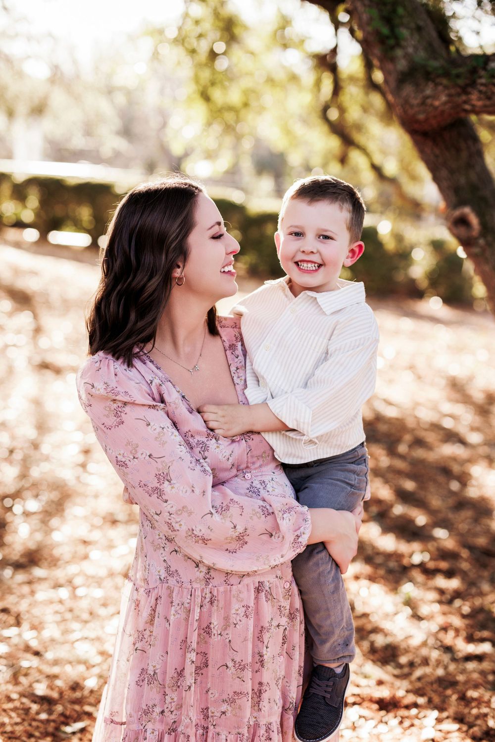 A loving moment captured outdoors in autumn sunlight with a pink floral dress and casual attire.