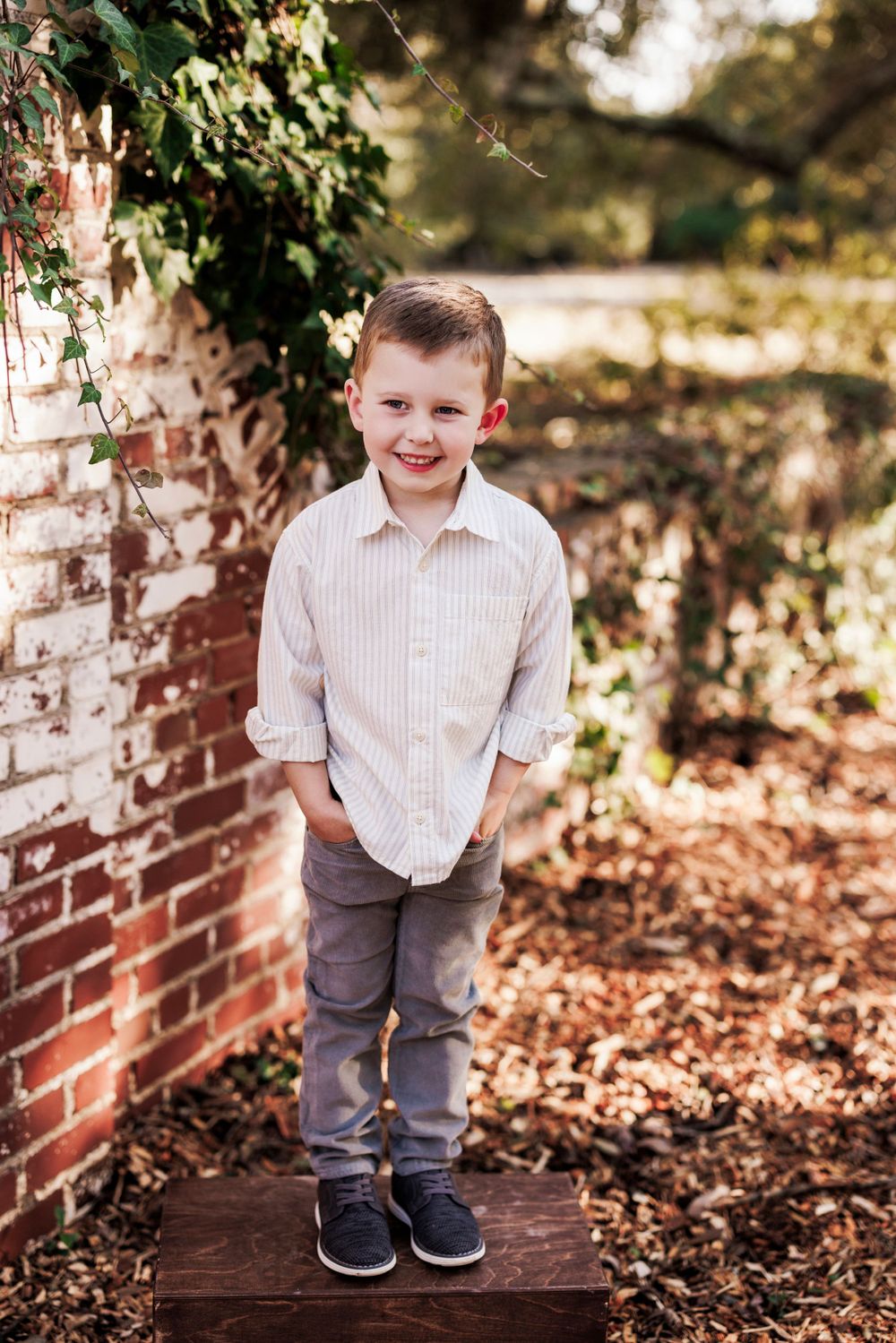 Joyful pose outdoors by a brick wall with fallen autumn leaves and natural lighting.