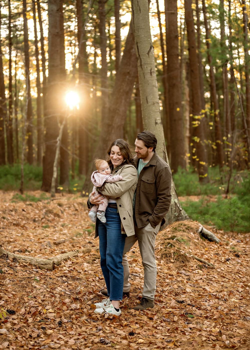 A couple shares a romantic moment among fallen autumn leaves in a sunlit forest during golden hour.