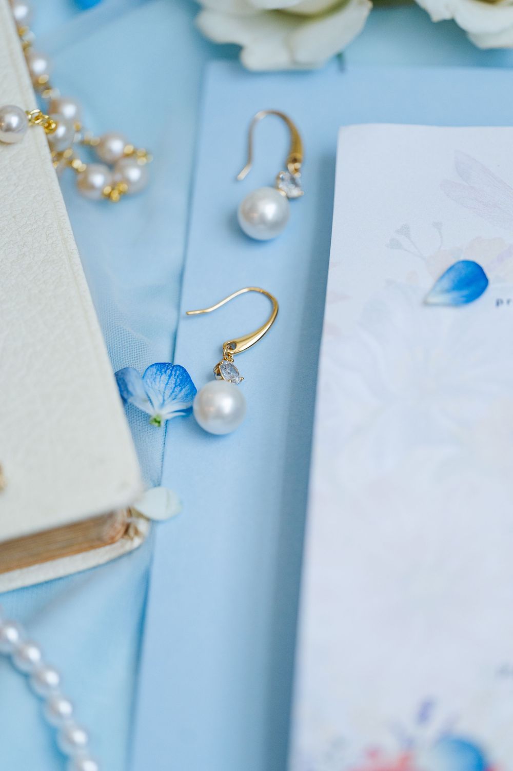 Wedding Jewelry and florals on a blue background for a Catholic, pastel summer wedding.