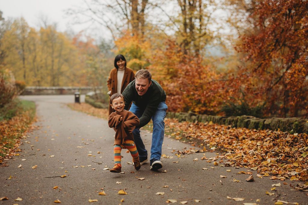 People walk together on a winding path surrounded by vibrant fall foliage and scattered autumn leaves.