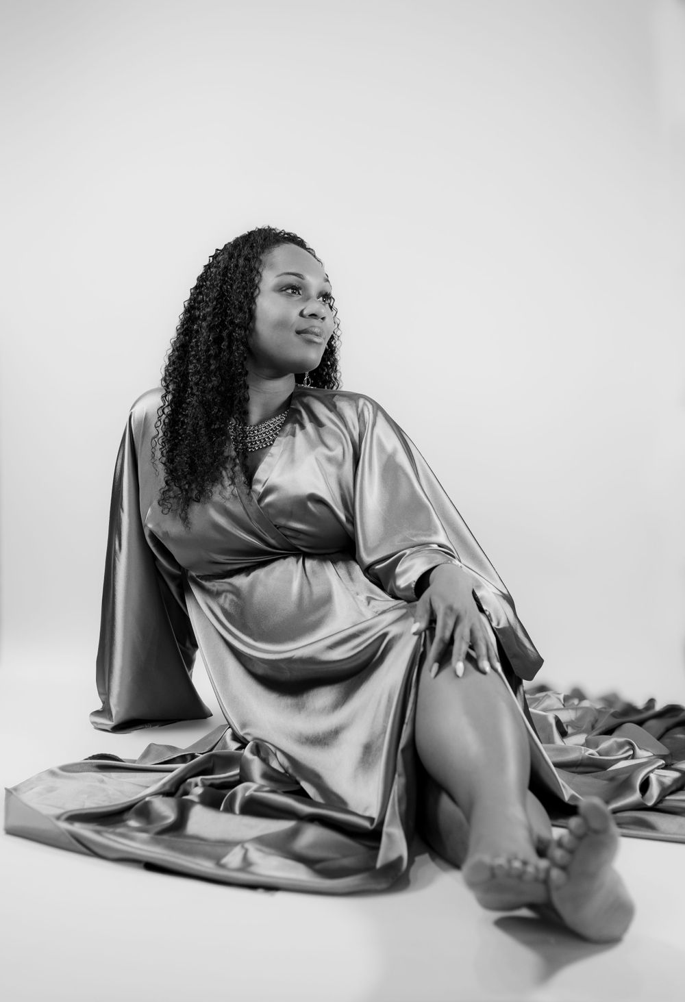 Black and white portrait of someone in a flowing silk robe lounging on the floor in an artistic pose.