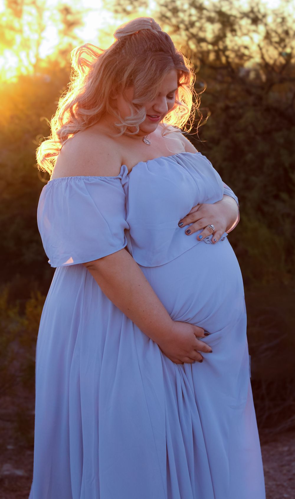 Expecting mother in off-shoulder blue dress poses during golden hour sunset.