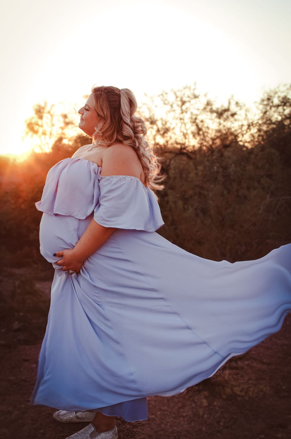 Woman in flowing lavender dress twirls during sunset in an outdoor maternity photoshoot.