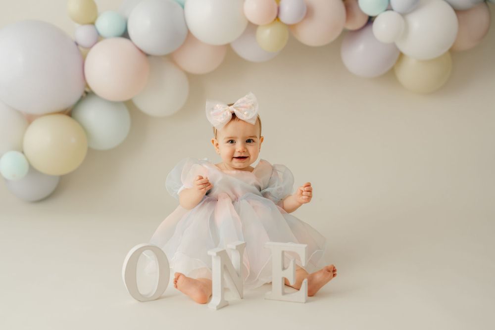 First birthday celebration with pastel balloon arch and 'ONE' letters on floor.