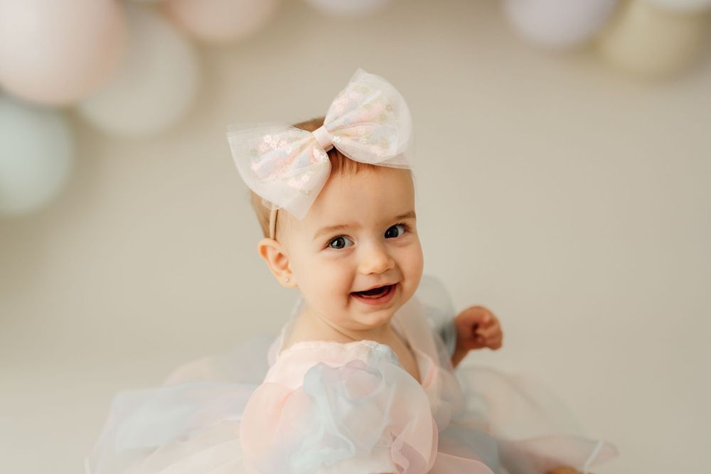 Sweet first birthday portrait with pastel balloons and white tulle dress.