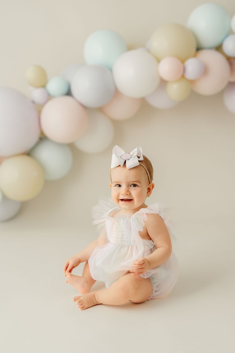 White dress and bow against pastel balloon backdrop for birthday photoshoot.