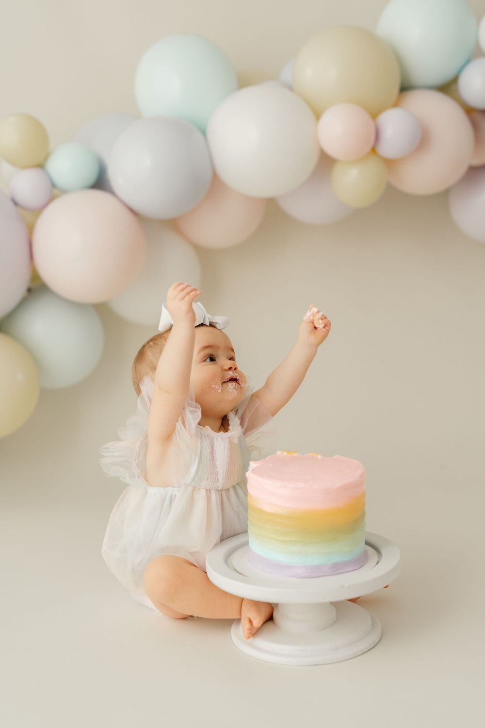 Joyful cake smash photography session with pastel balloons and rainbow birthday cake.