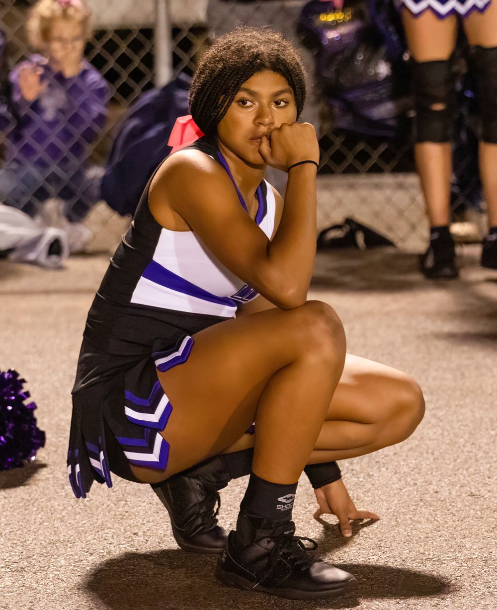 Cheerleader in black and purple uniform crouches on sideline during game.
cheer kanawha county riverside